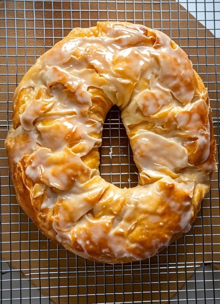 Freshly baked Wisconsin Apple Kringle with vanilla glaze cooling on a wire rack.