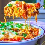 Cheesy chicken tamale pie slice being lifted from a casserole dish, topped with green onions and melted cheese